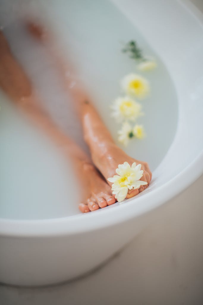 Close-up of feet soaking in a bathtub with yellow flowers, evoking relaxation and pampering.