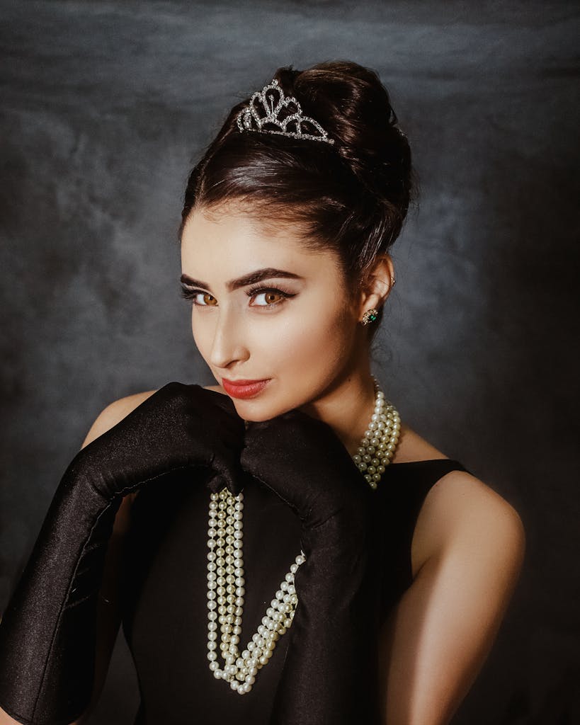 Portrait of a woman wearing a tiara, black dress, and pearls, exuding elegance.